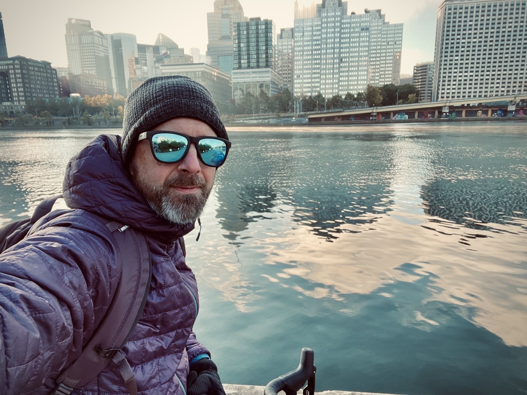 A man in a beanie on a bike with a river and the city of Pittsburgh in the background