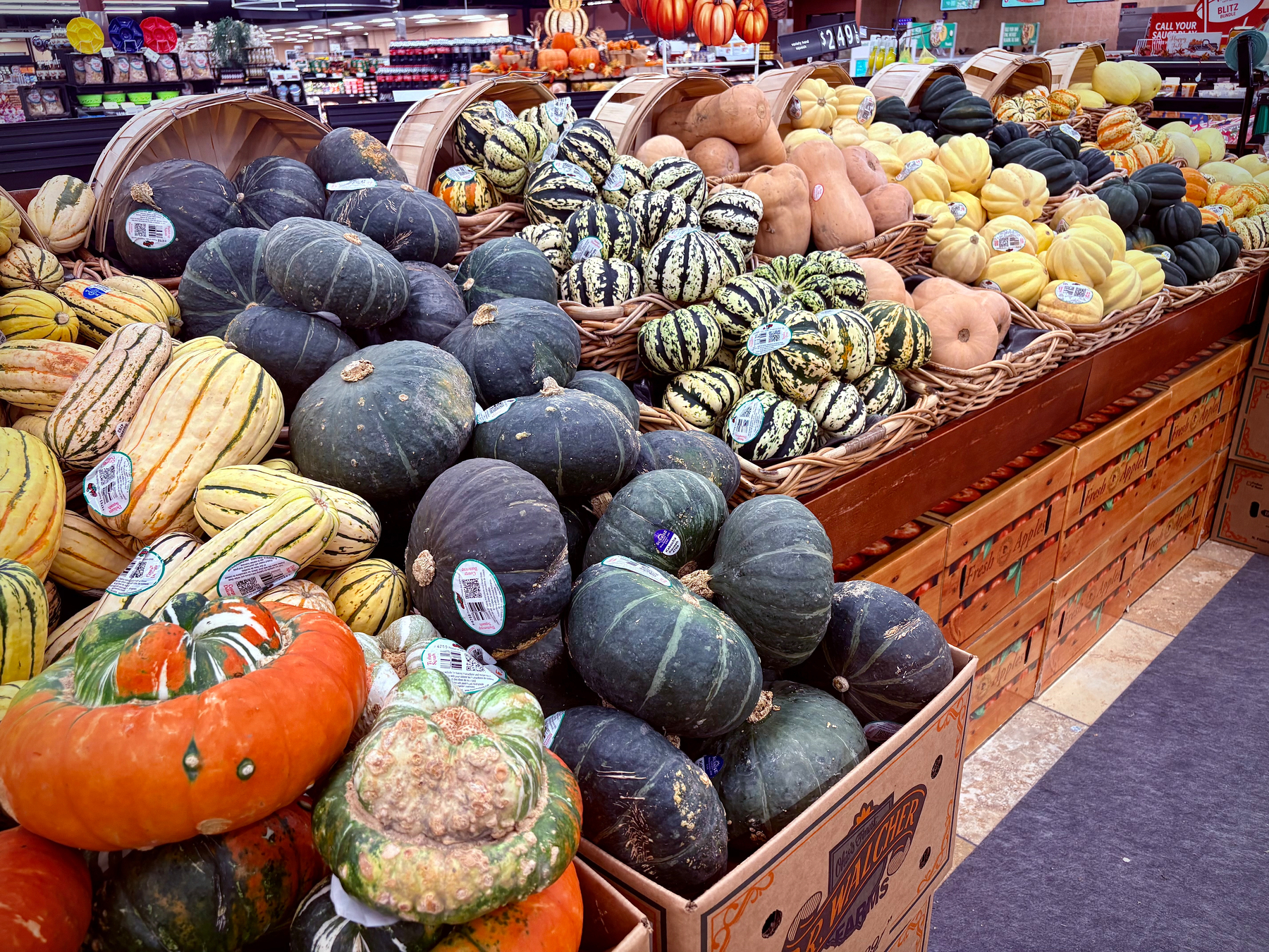 A variety of colorful pumpkins and squash are displayed in wooden crates at a grocery store.