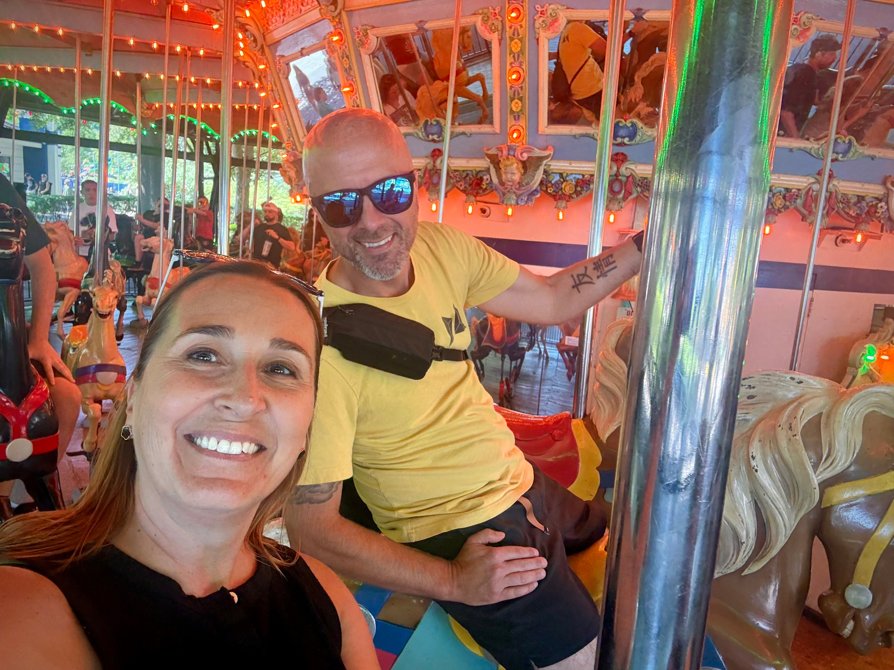 A woman and a man are smiling and enjoying their time on a brightly lit carousel.