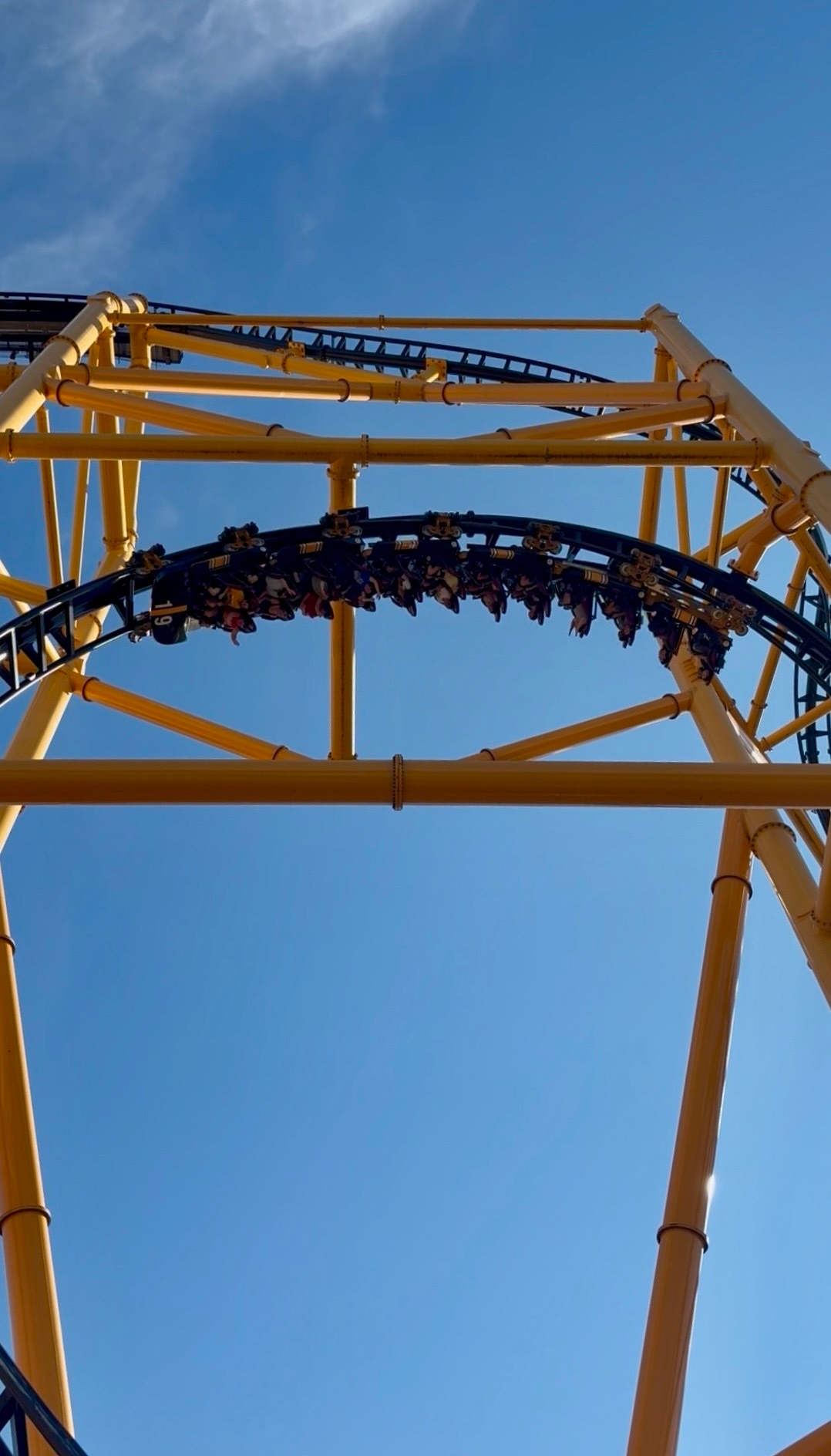 A roller coaster with yellow supports and black tracks is captured mid-loop against a clear blue sky.
